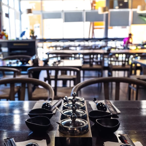 A restaurant table set with condiment containers, small bowls, and utensils, with a blurred dining area in the background.