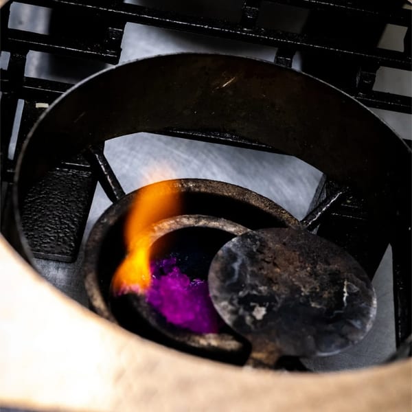A small burner with a purple substance and a bright orange flame, viewed from above.