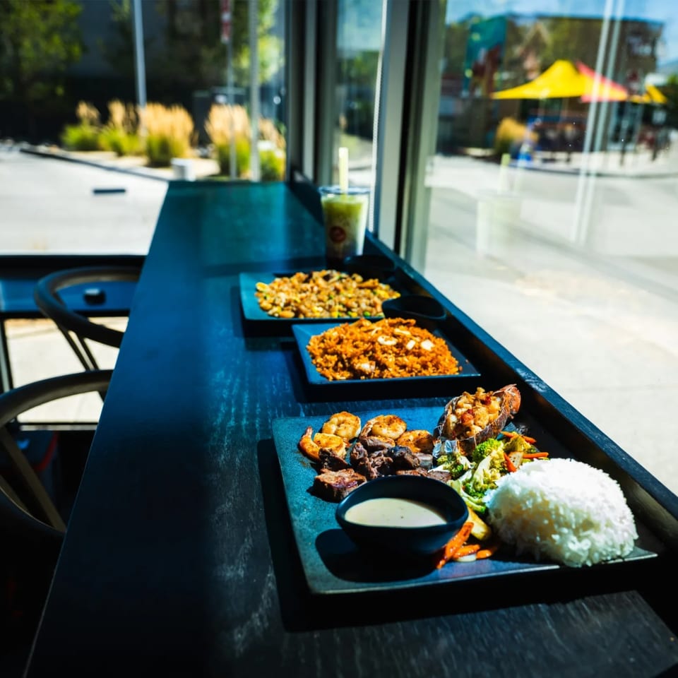 Fried rice, seafood rice, and a surf and turf platter lined up on a window counter