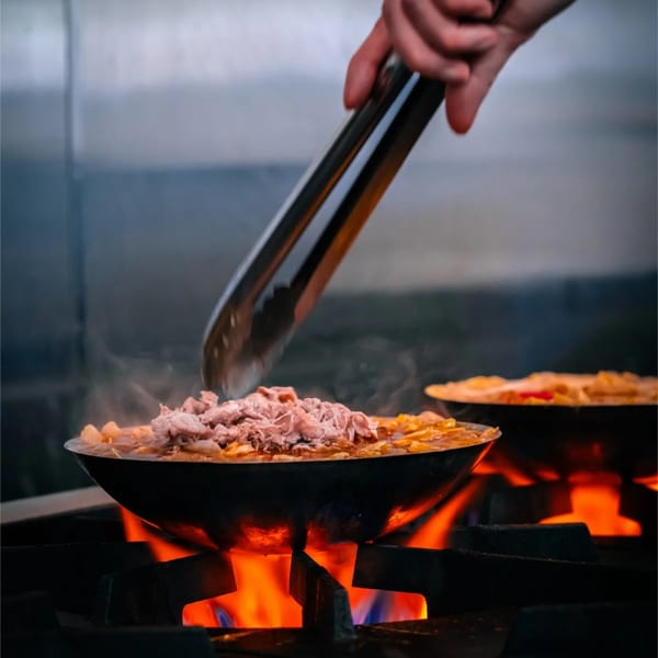 Cook using tongs over a hot pot on an open flame with a second pot behind