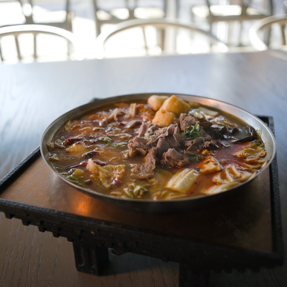 Hot pot with beef on a stand with white chairs behind