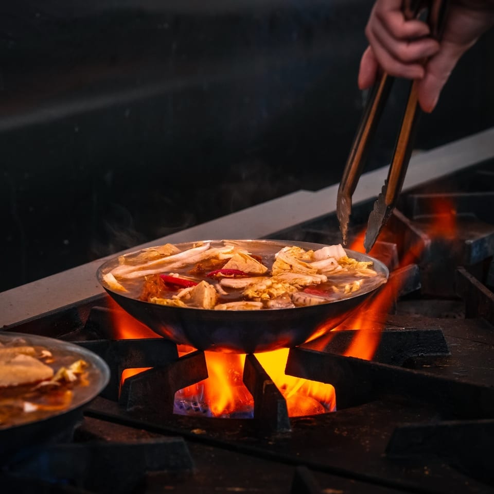 Hot pot cooking over blue and orange flame with tongs