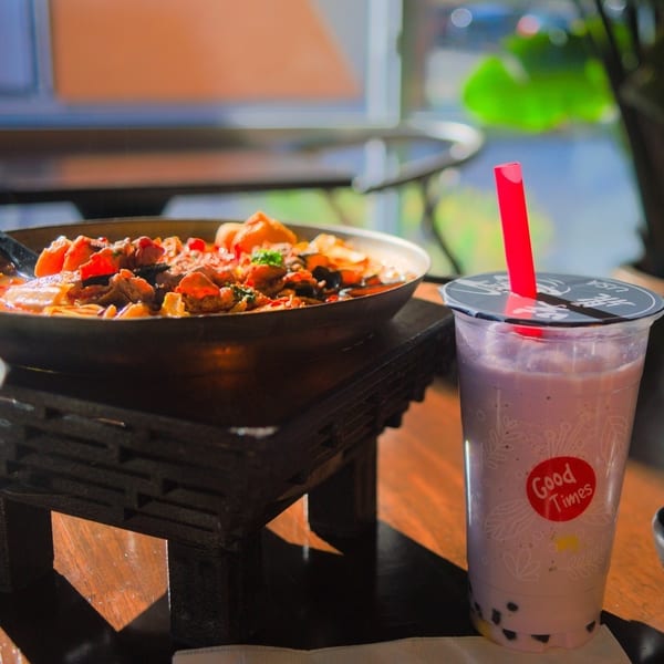 A colorful dish with meat and vegetables in a pan next to a taro bubble tea.