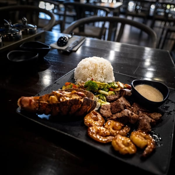 Surf and turf platter with lobster tail, steak, shrimp and rice on a black plate