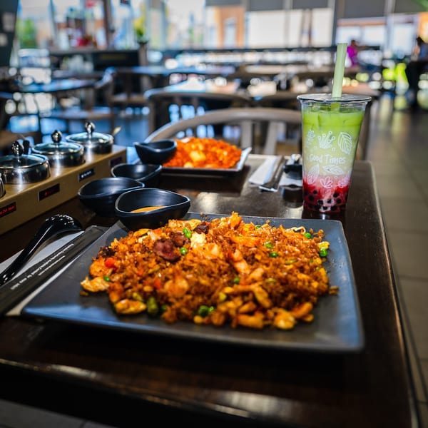 A plate of fried rice with shrimp and beef, a green bubble tea, and small sauce dishes on a table.