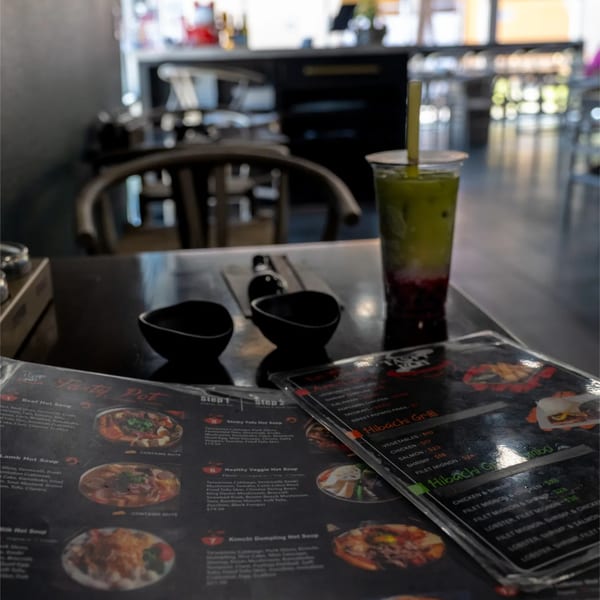 A restaurant table with menus, two small black bowls, and a green and red layered drink.